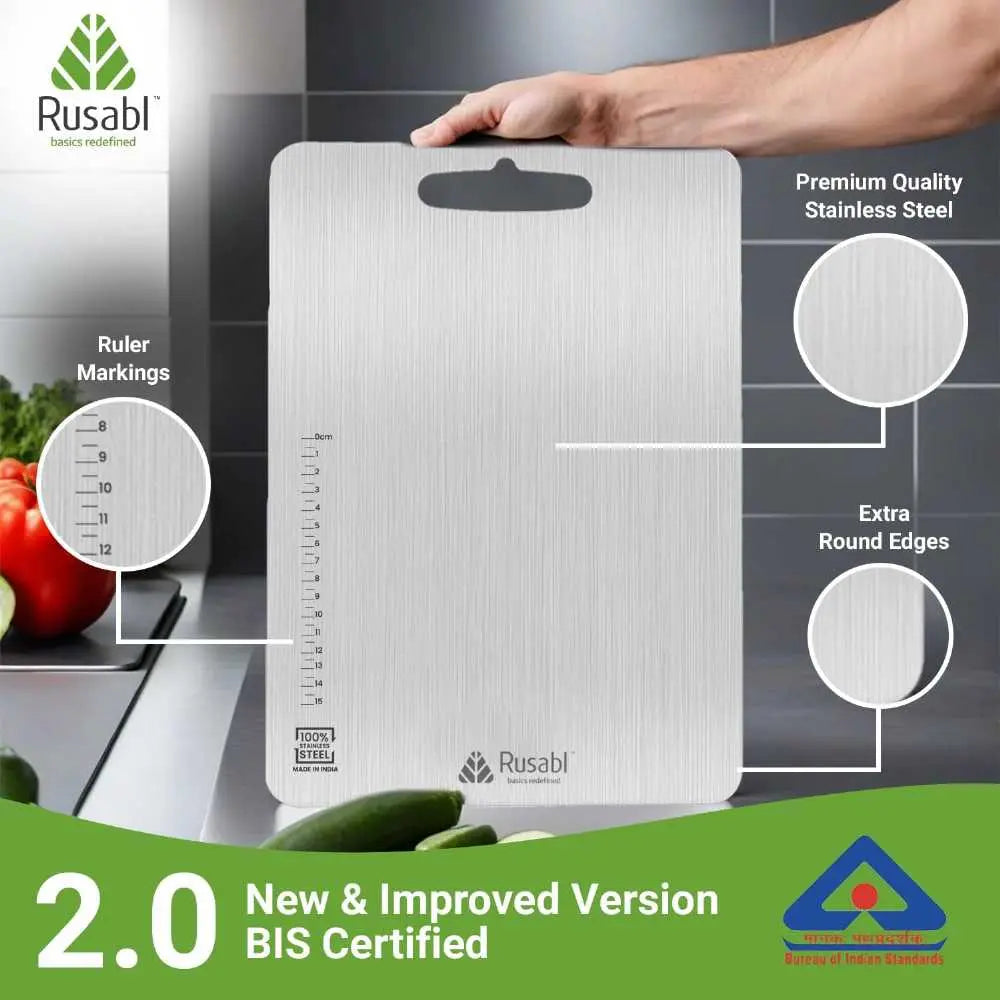 A brushed stainless steel kitchen cutting board with a built-in handle, shown being held by a hand. The image includes callout circles and text highlighting ruler markings, premium stainless steel, extra round edges, and BIS certification, with the Rusabl brand visible.