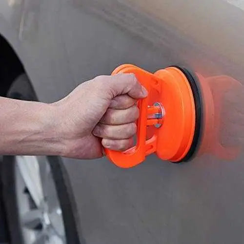 Person using an orange car dent removal tool on a car door.